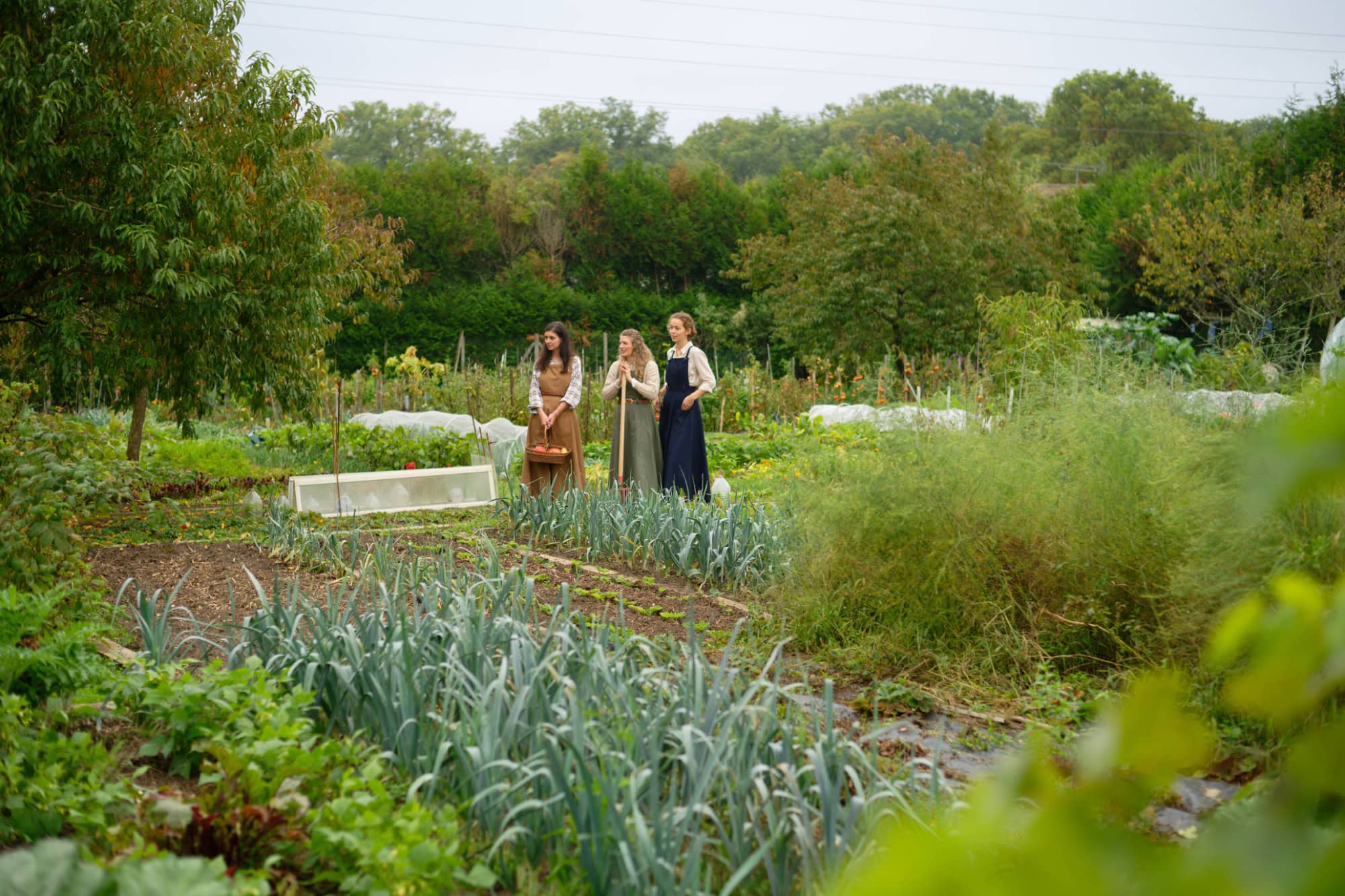 Trois modèles en robes salopettes bleu, camel et kaki dans un potager
